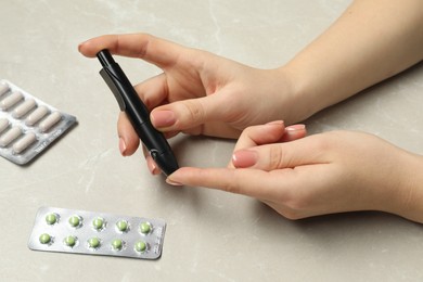 Diabetes. glucose testing. Woman using lancet pen at light table, closeup