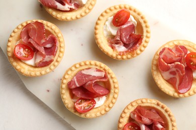 Delicious canapes with jamon, cream cheese and cherry tomatoes on white table, top view