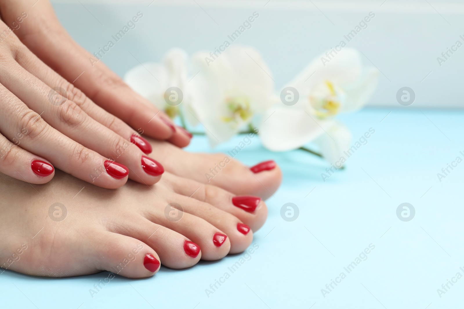 Photo of Woman with stylish red toenails after pedicure procedure on light blue background, closeup. Space for text