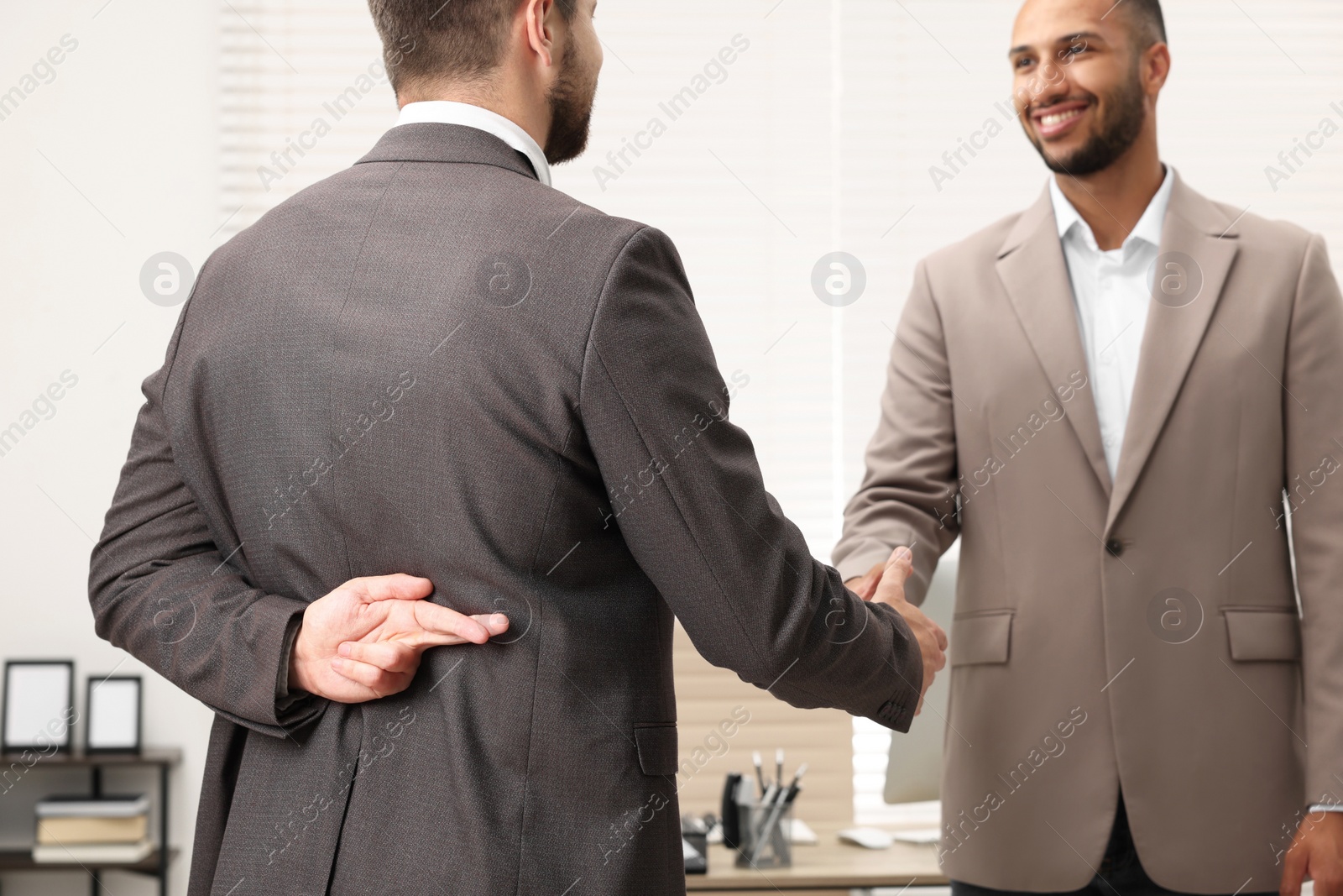 Photo of Employee crossing fingers behind his back while shaking hands with boss in office