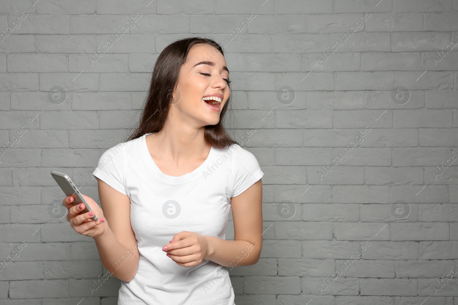 Photo of Attractive young woman using mobile phone on brick wall background