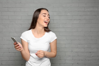 Attractive young woman using mobile phone on brick wall background