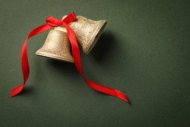 Bells with red bow on dark green background, flat lay. Space for text. Christmas decor