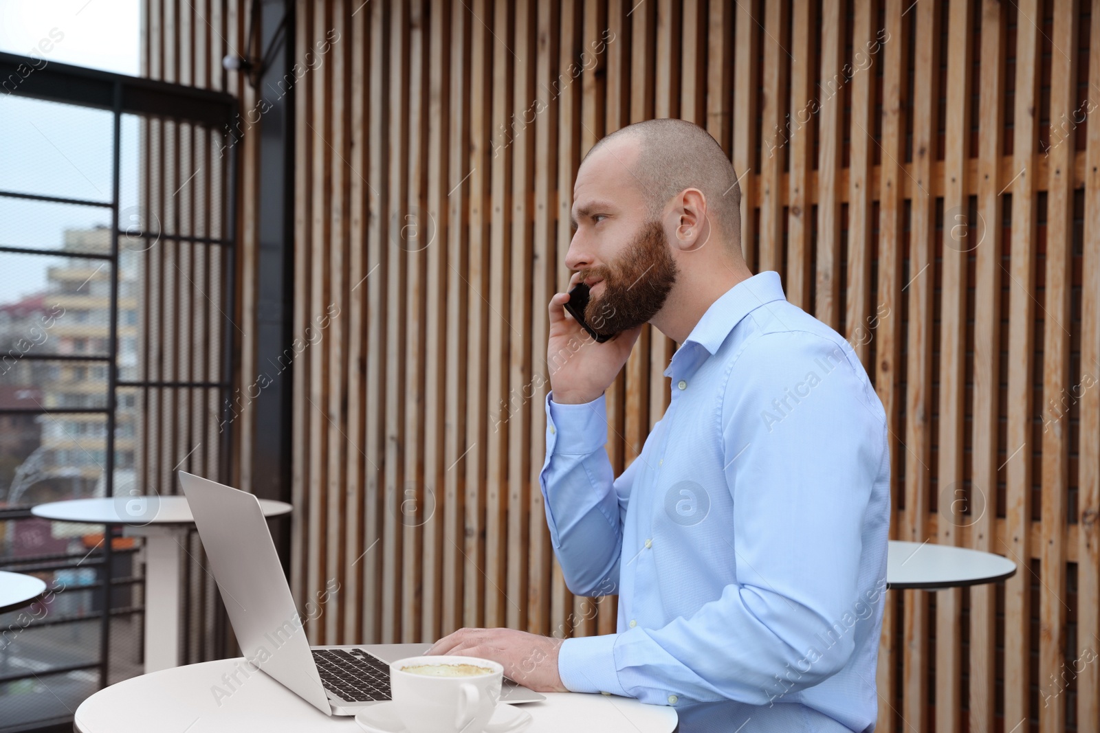 Photo of Businessman with laptop talking on phone in outdoor cafe. Corporate blog