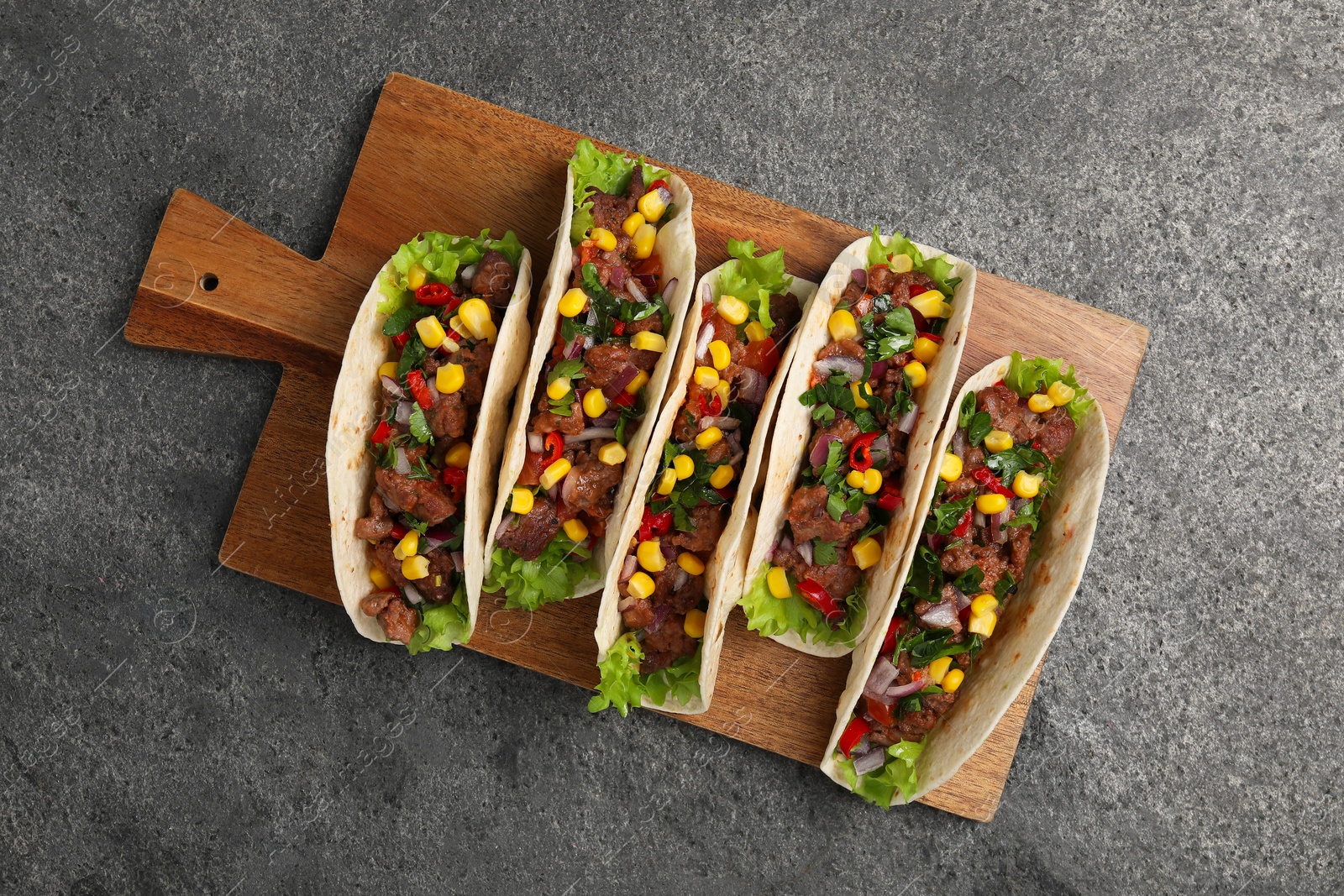 Photo of Delicious tacos with meat and vegetables on gray textured table, top view