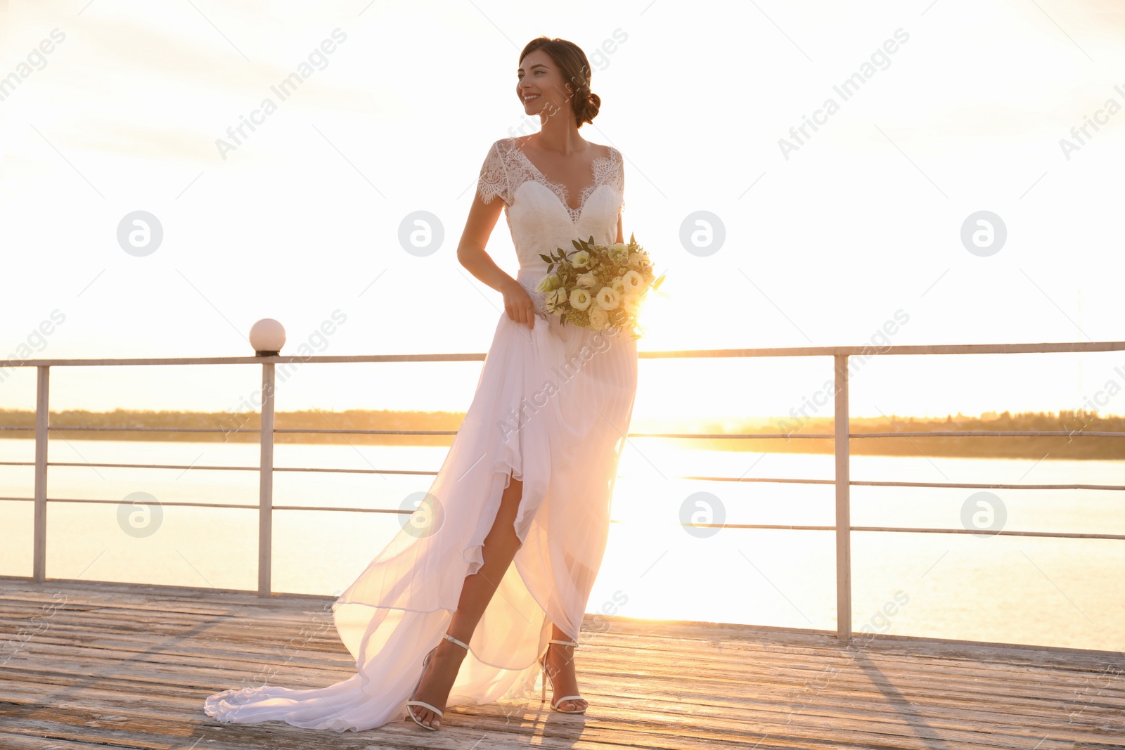 Photo of Gorgeous bride in beautiful wedding dress with bouquet near river on sunset