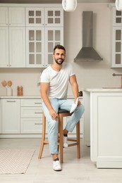 Photo of Handsome man with notebook sitting on stool in kitchen