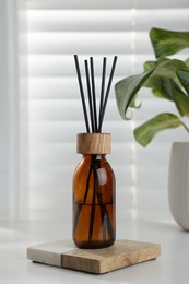 Air reed freshener and houseplant on white table near window