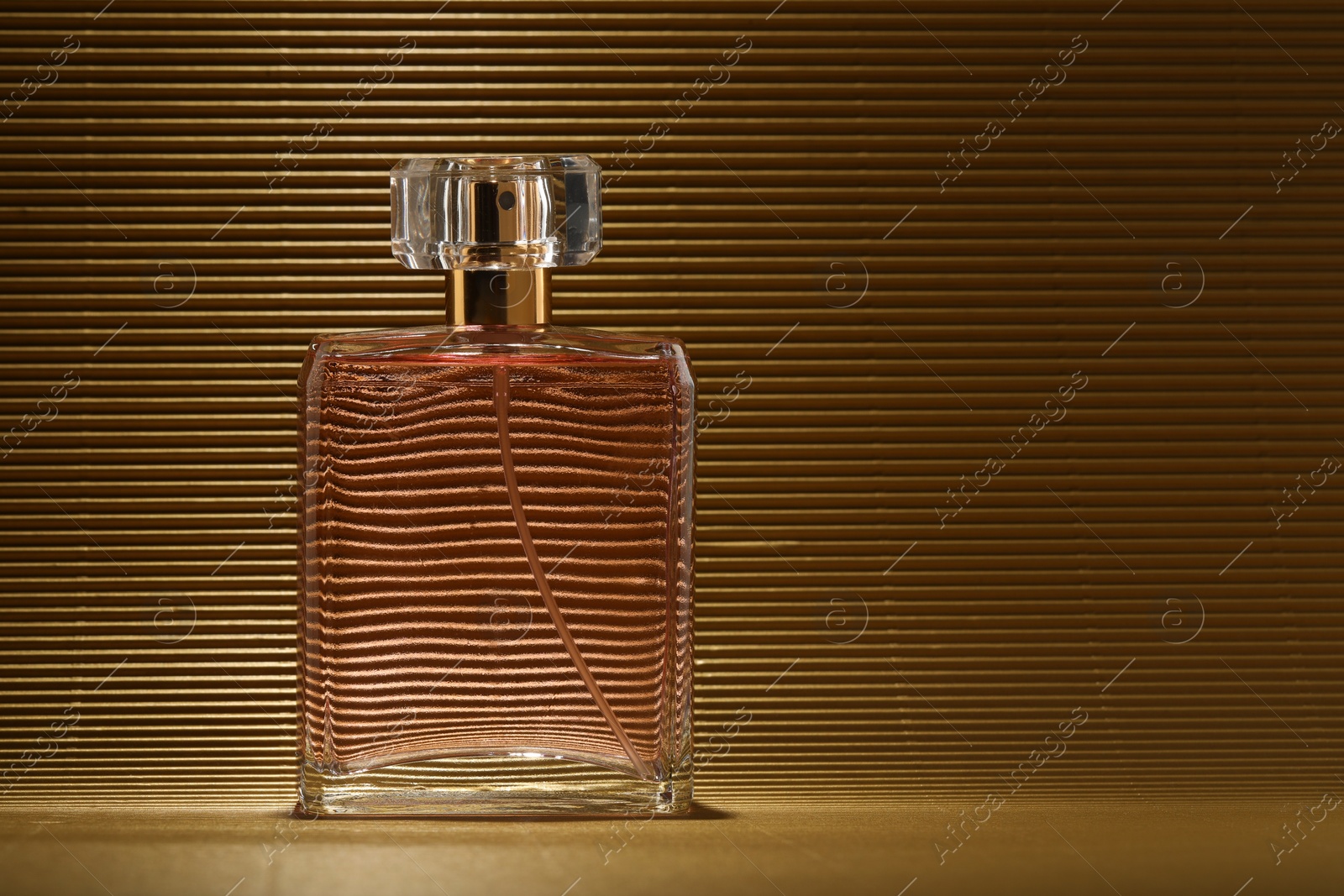 Photo of Luxury women's perfume. Sunlit glass bottle on golden surface, space for text