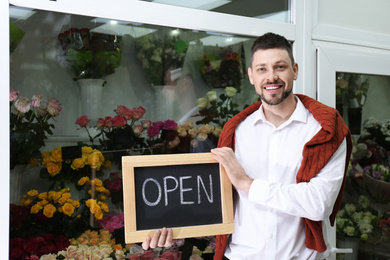 Photo of Male business owner holding OPEN sign in his flower shop