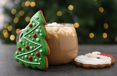 Photo of Decorated cookies and hot drink on grey table against blurred Christmas lights