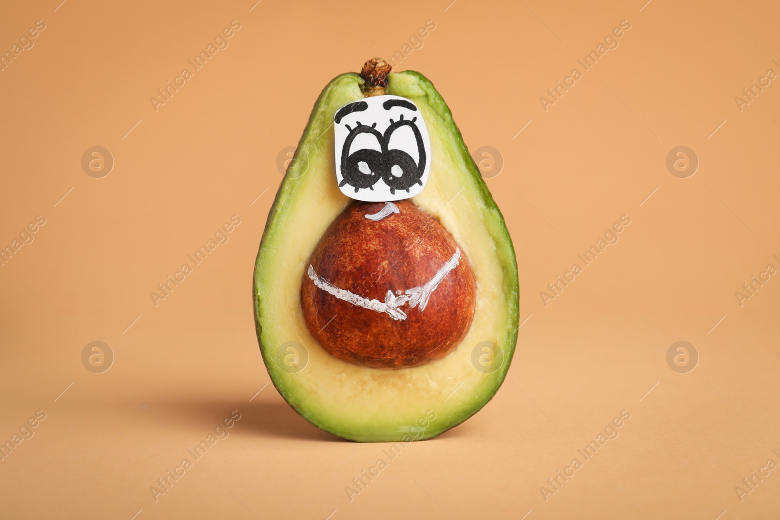 Photo of Avocado with drawn face on orange background. Exhibitionist concept
