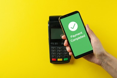 Image of Woman using terminal for contactless payment with smartphone on yellow background, top view. Transaction completed screen on device