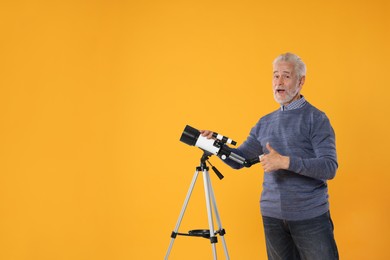 Senior astronomer with telescope showing thumb up on yellow background, space for text