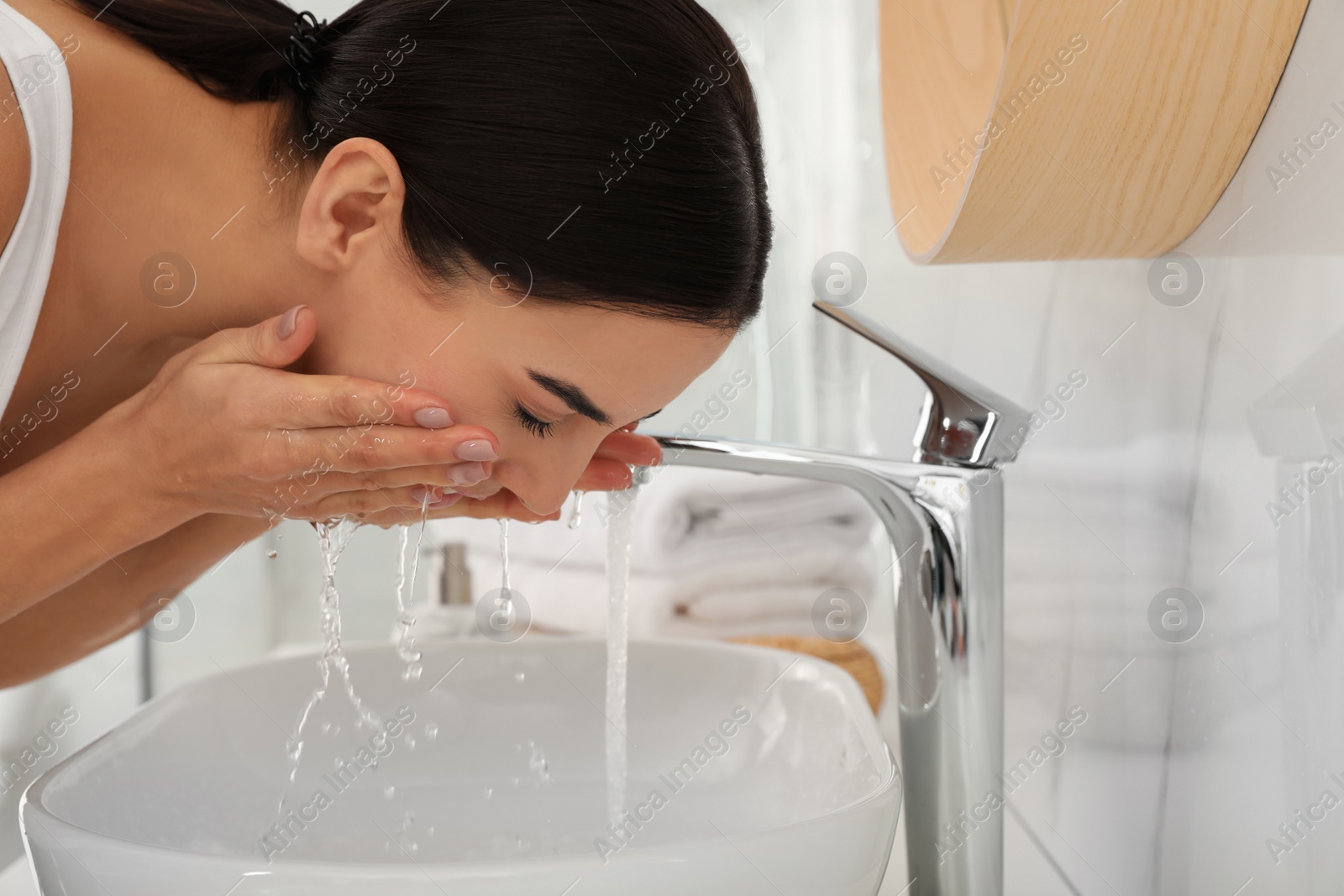 Photo of Young woman washing face with cosmetic product in bathroom