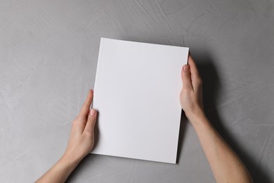 Woman holding notebook with blank cover at light grey table, top view. Mockup for design