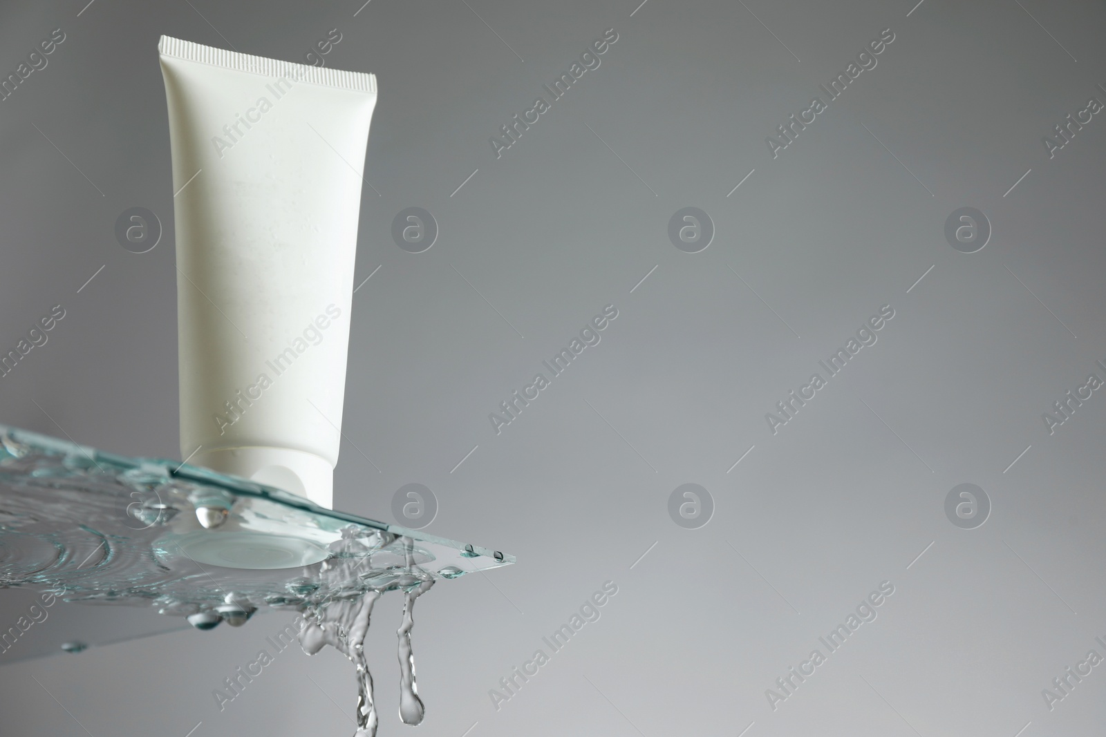 Photo of Tube with moisturizing cream on glass against grey background, low angle view. Space for text