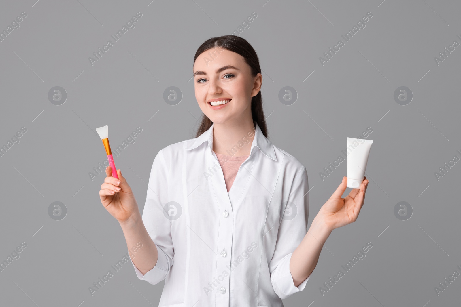 Photo of Cosmetologist with cosmetic product and silicone brush on grey background