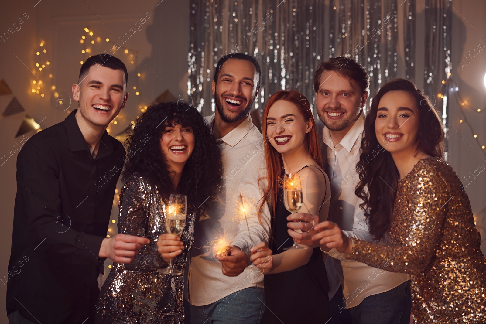 Photo of Happy friends with glasses of wine and sparklers celebrating birthday indoors