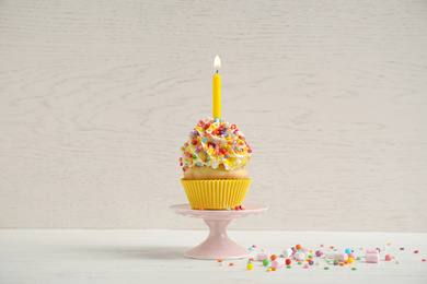 Photo of Birthday cupcake with candle on white table against wooden background