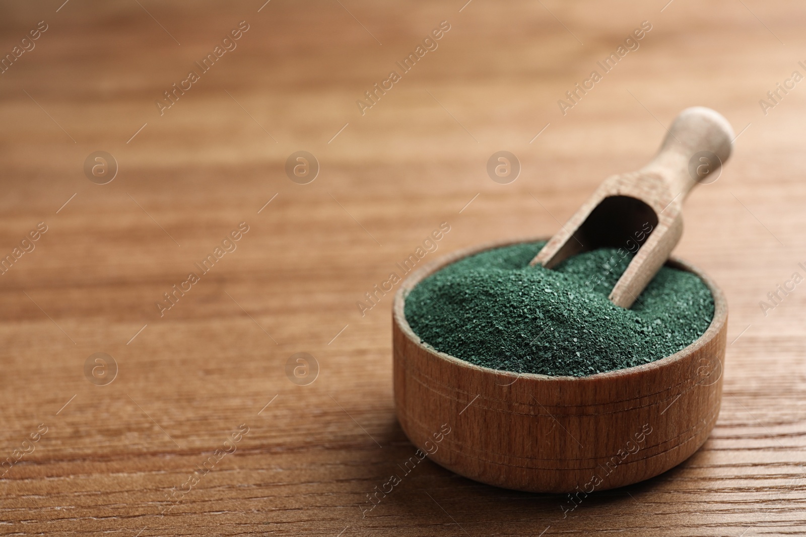 Photo of Scoop in bowl of spirulina powder on wooden table. Space for text