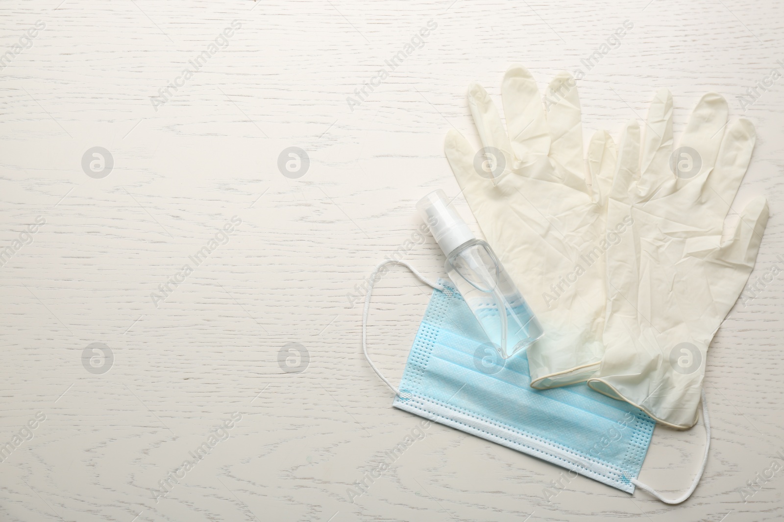 Photo of Medical gloves, protective mask and hand sanitizer on white wooden background, flat lay. Space for text