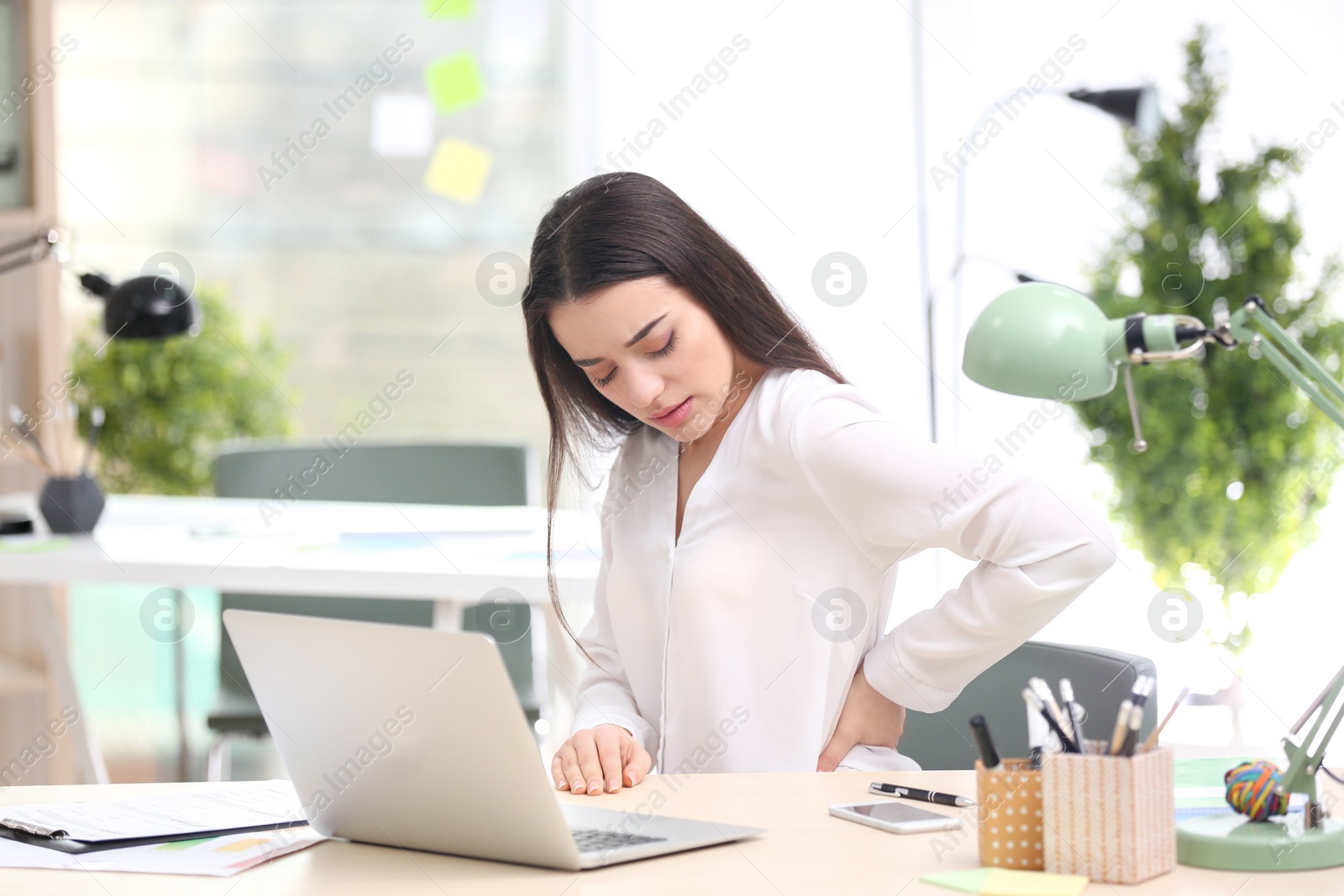 Photo of Young woman suffering from back pain in office