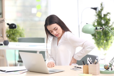 Photo of Young woman suffering from back pain in office