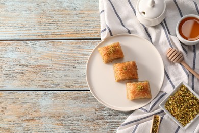 Photo of Delicious sweet baklava with nuts and honey on light blue wooden table, flat lay. Space for text