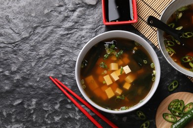 Photo of Delicious miso soup with tofu served on black textured table, flat lay. Space for text