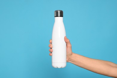 Photo of Woman holding thermo bottle of drink on light blue background, closeup