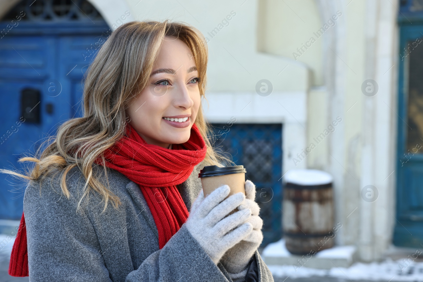 Photo of Portrait of smiling woman with paper cup of coffee on city street in winter. Space for text