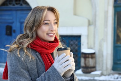 Photo of Portrait of smiling woman with paper cup of coffee on city street in winter. Space for text