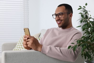 Photo of Happy man sending message via smartphone at home