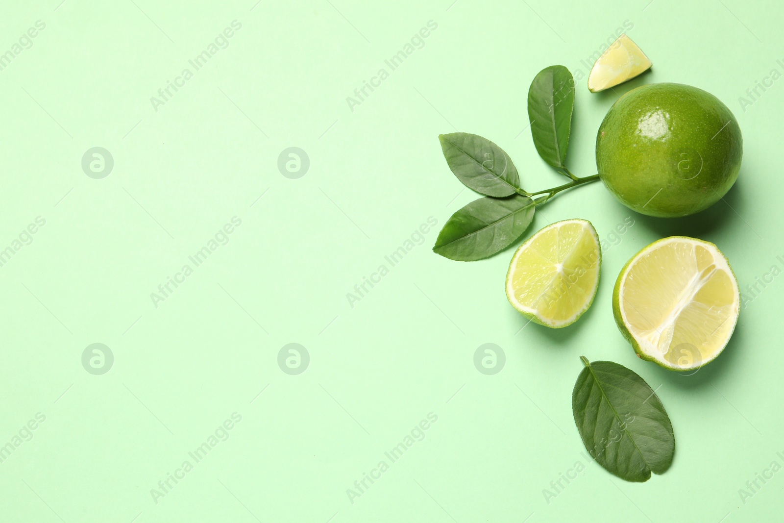 Photo of Whole and cut fresh ripe limes with leaves on light green background, flat lay