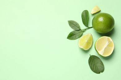 Whole and cut fresh ripe limes with leaves on light green background, flat lay