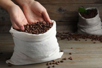 Photo of Woman taking roasted coffee beans from bag at wooden table, closeup. Space for text