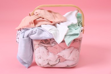 Photo of Laundry basket with baby clothes on light pink background