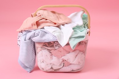 Laundry basket with baby clothes on light pink background