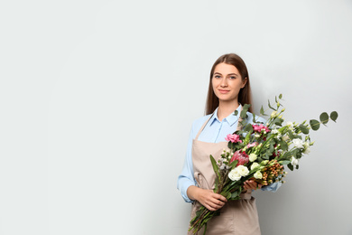 Photo of Florist with beautiful bouquet on light background, space for text