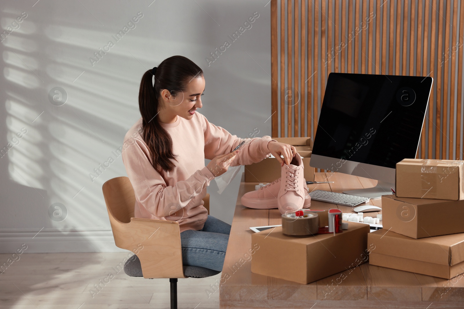 Photo of Shoes seller taking picture of pink sneakers at table in office. Online store