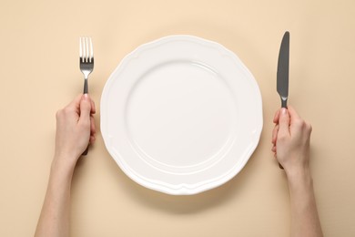 Photo of Woman with cutlery and empty plate at beige table, top view