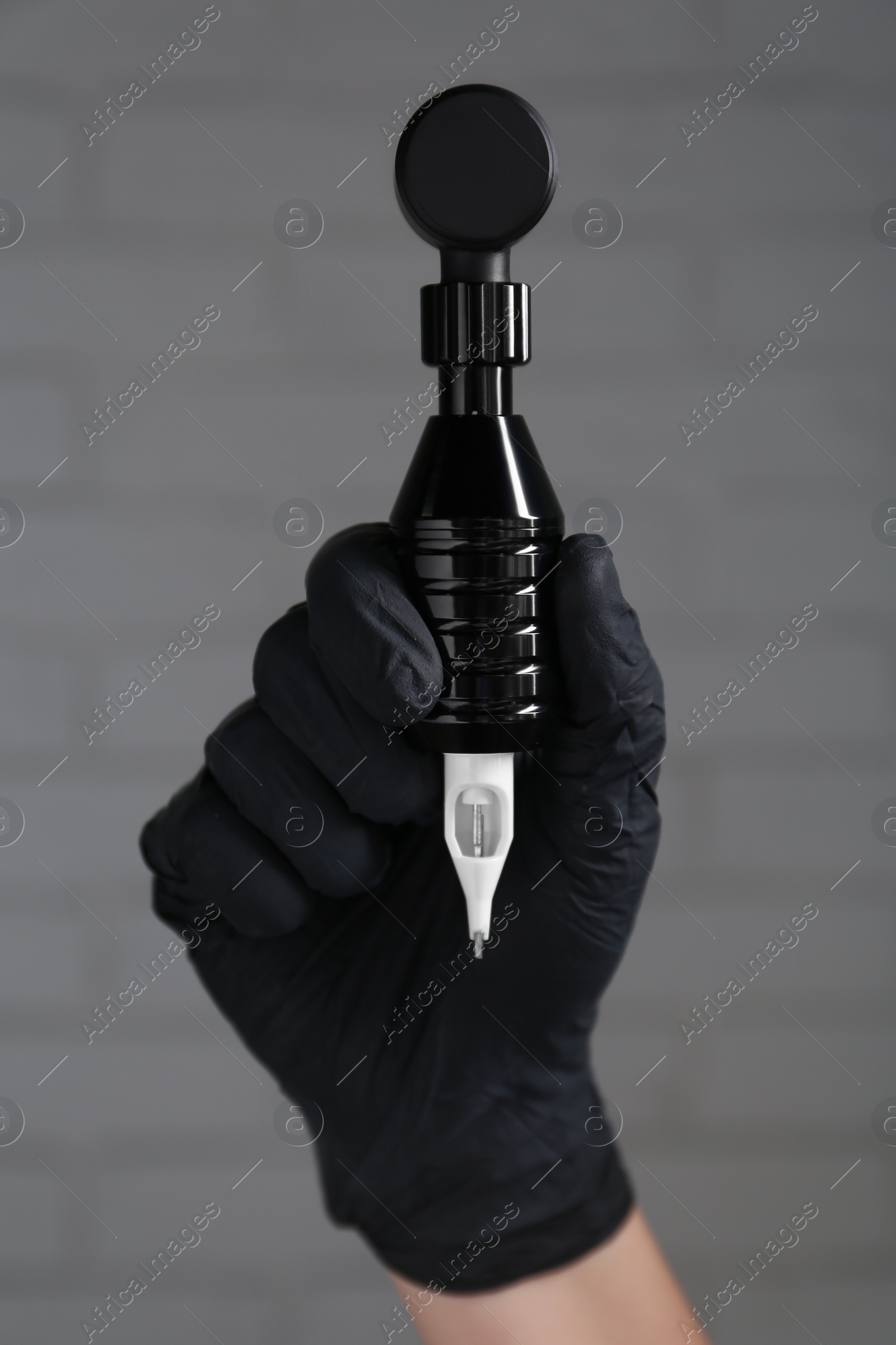 Photo of Professional tattoo artist with machine near white brick wall, closeup