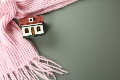 Photo of Wooden house model and pink scarf on  grey background, top view with space for text. Heating efficiency