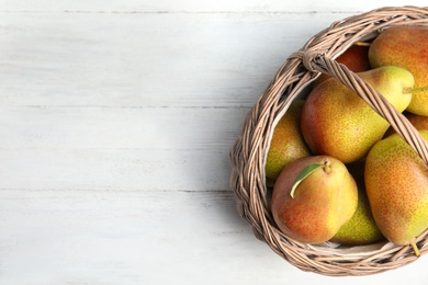 Photo of Ripe juicy pears in wicker basket on white wooden table, top view