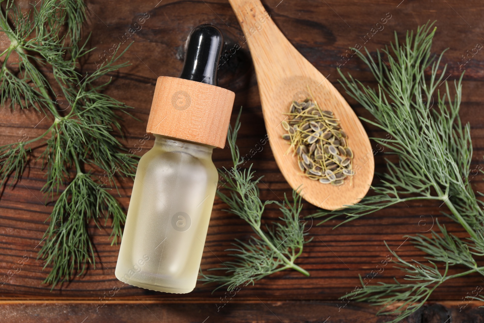 Photo of Bottle of essential oil and fresh dill on wooden table, flat lay