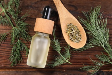 Bottle of essential oil and fresh dill on wooden table, flat lay