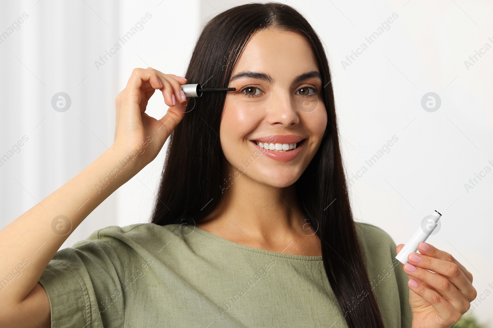 Photo of Beautiful woman applying serum onto her eyelashes in room. Cosmetic product