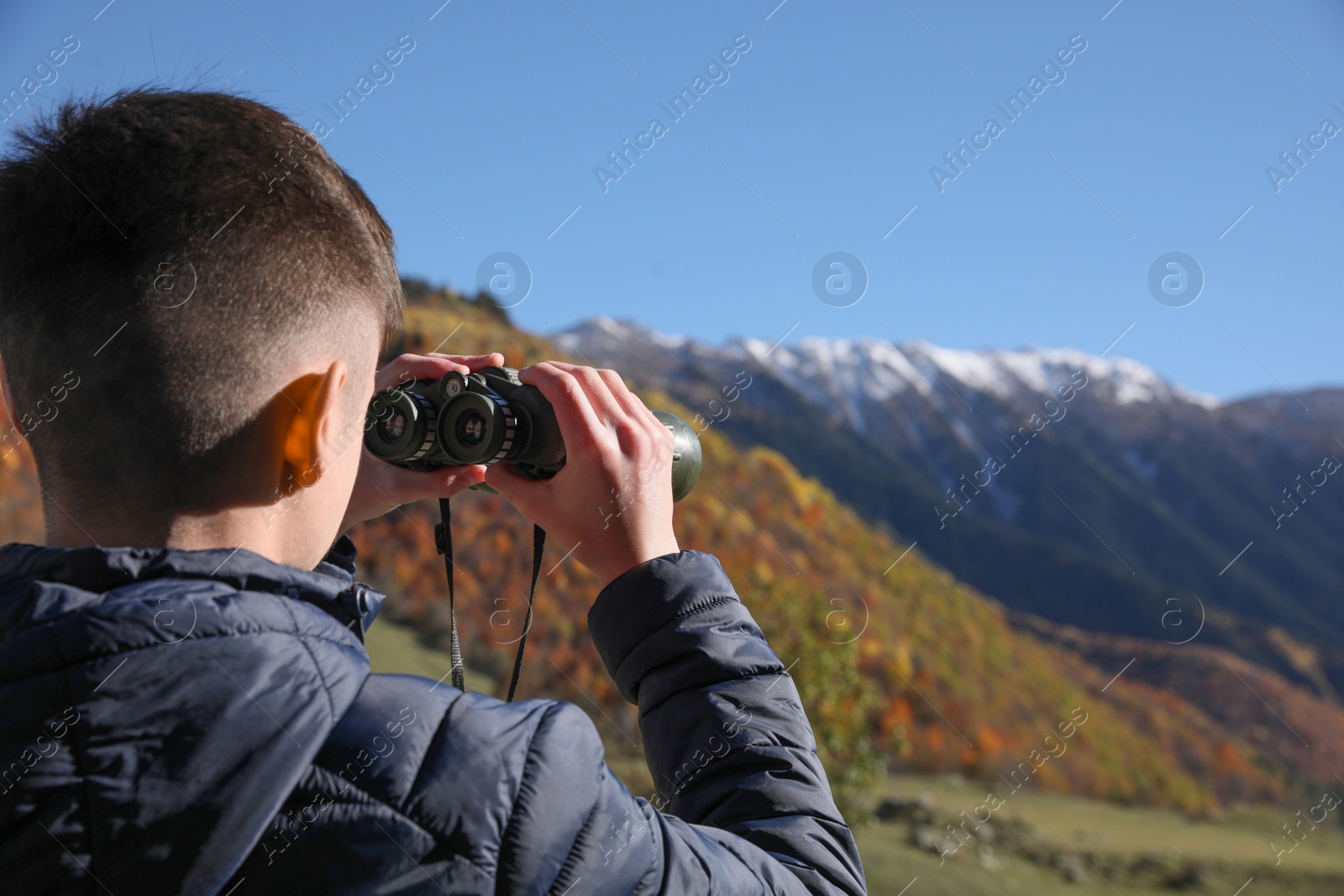 Photo of Boy looking through binoculars in mountains on sunny day. Space for text