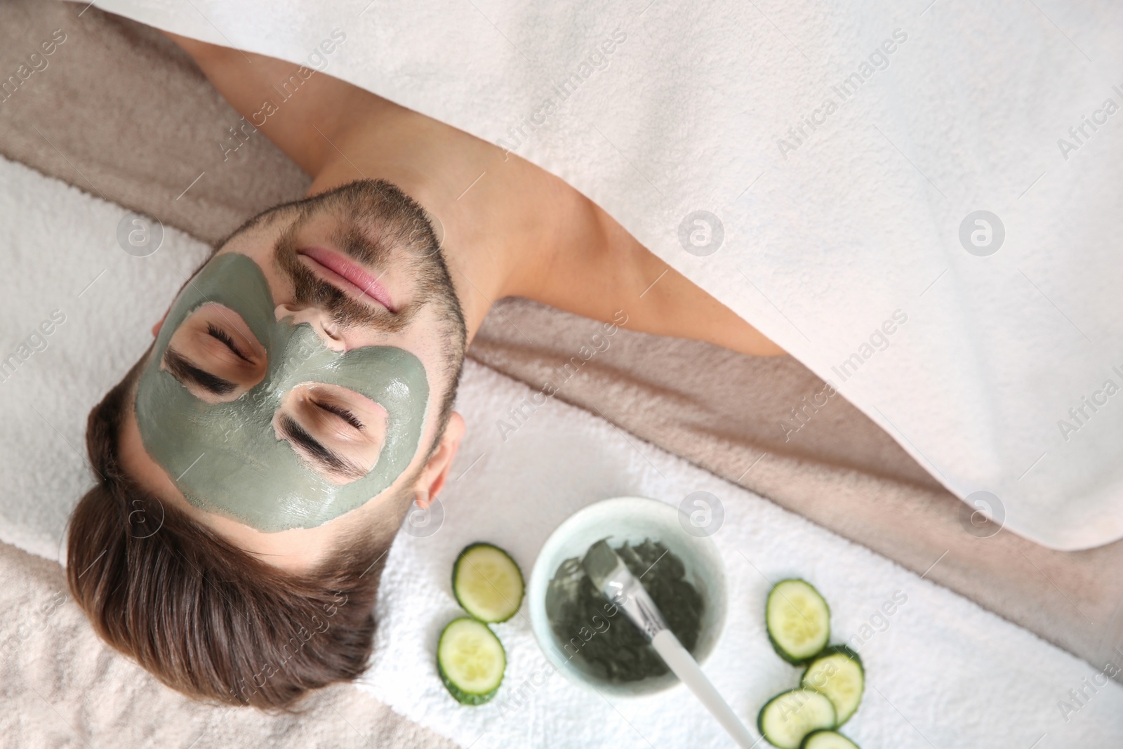 Photo of Young man with clay mask on his face in spa salon, above view